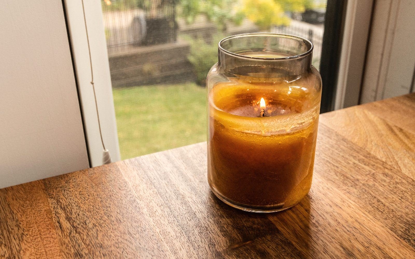 A lit amber candle in a glass jar by a window